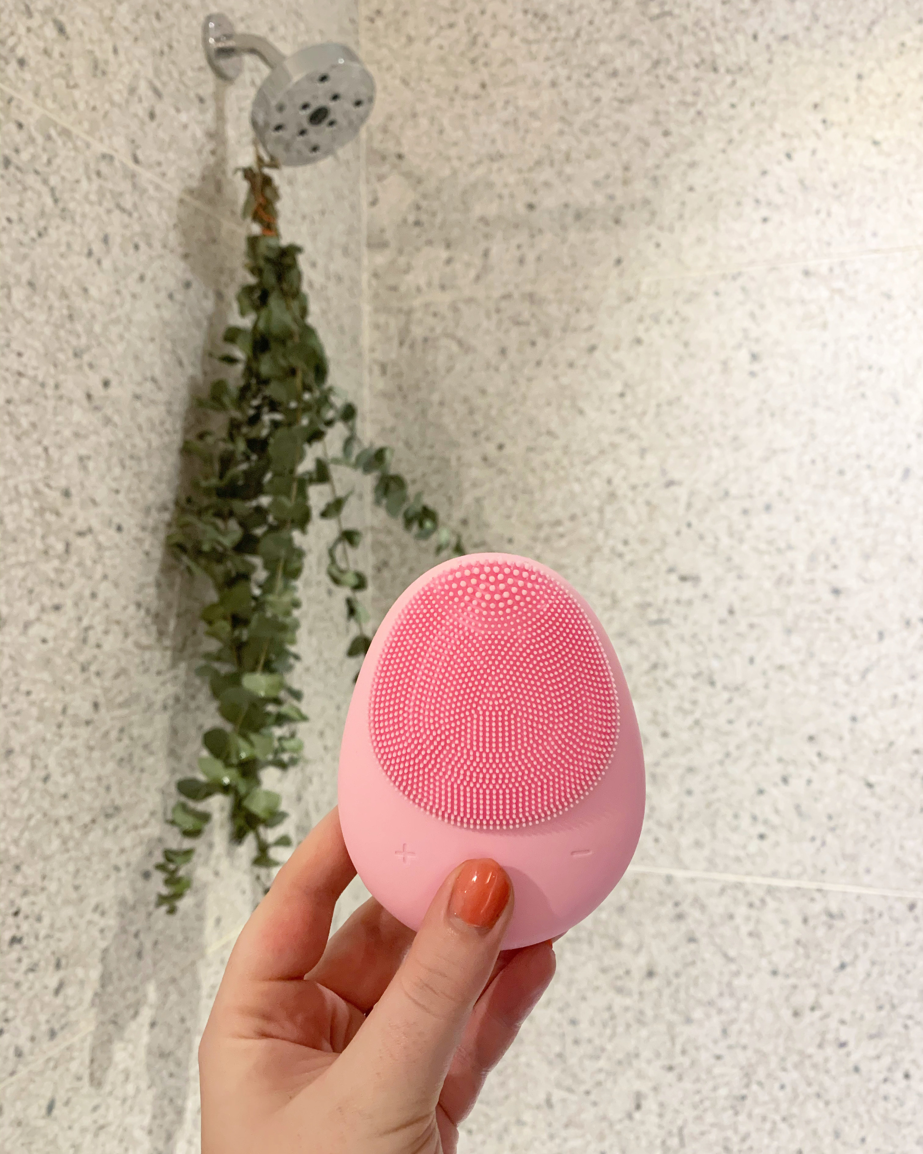 My hand holding up my palm-sized cleansing brush. It&#x27;s the shape of a flattened egg, with soft silicone bristles on both sides. 