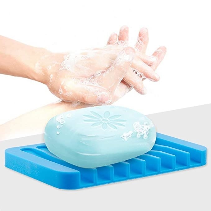 Blue soap on a blue silicone dish with a person washing their hands in the background