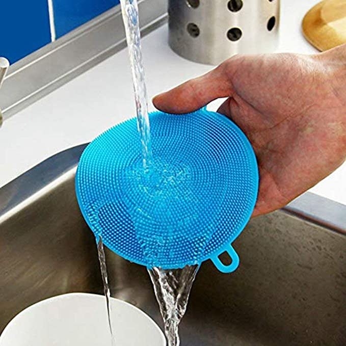 Blue silicone brush being washed in the sink under a running tap