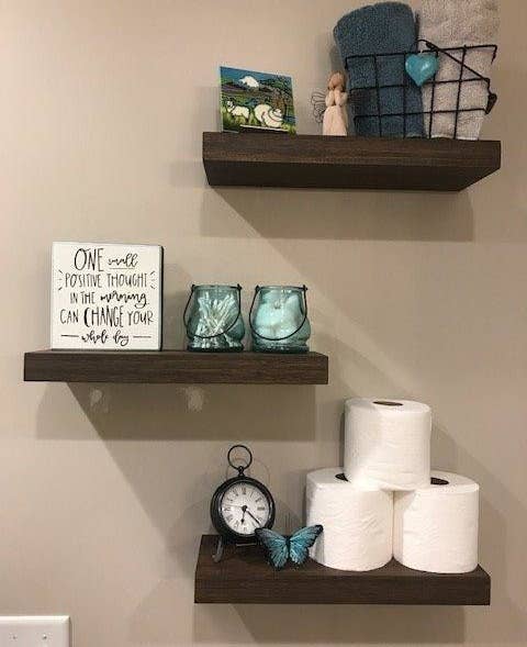 reviewer photo of three shelves in the bathroom with toilet paper, candles, and towels on them