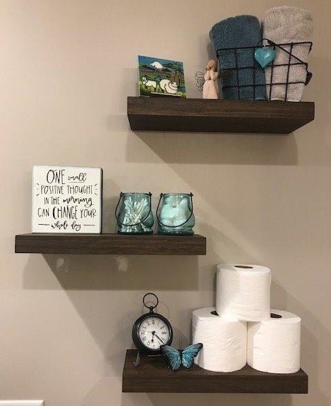 reviewer photo of three shelves in the bathroom with toilet paper, candles, and towels on them