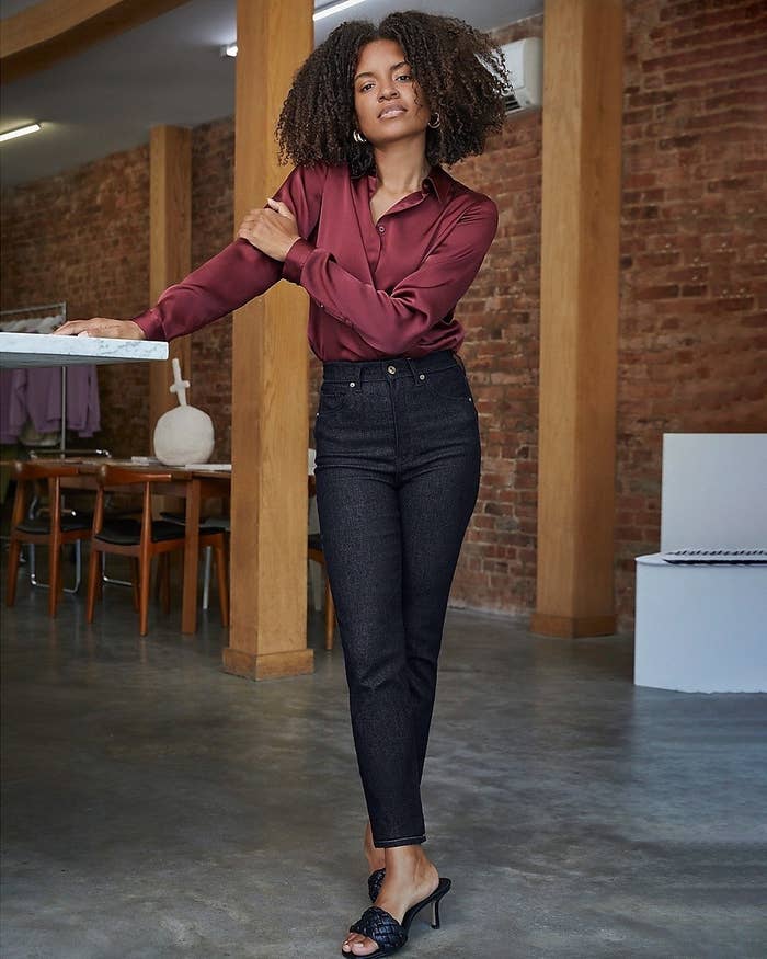 A model wearing the burgundy long-sleeved shirt tucked into dark wash jeans