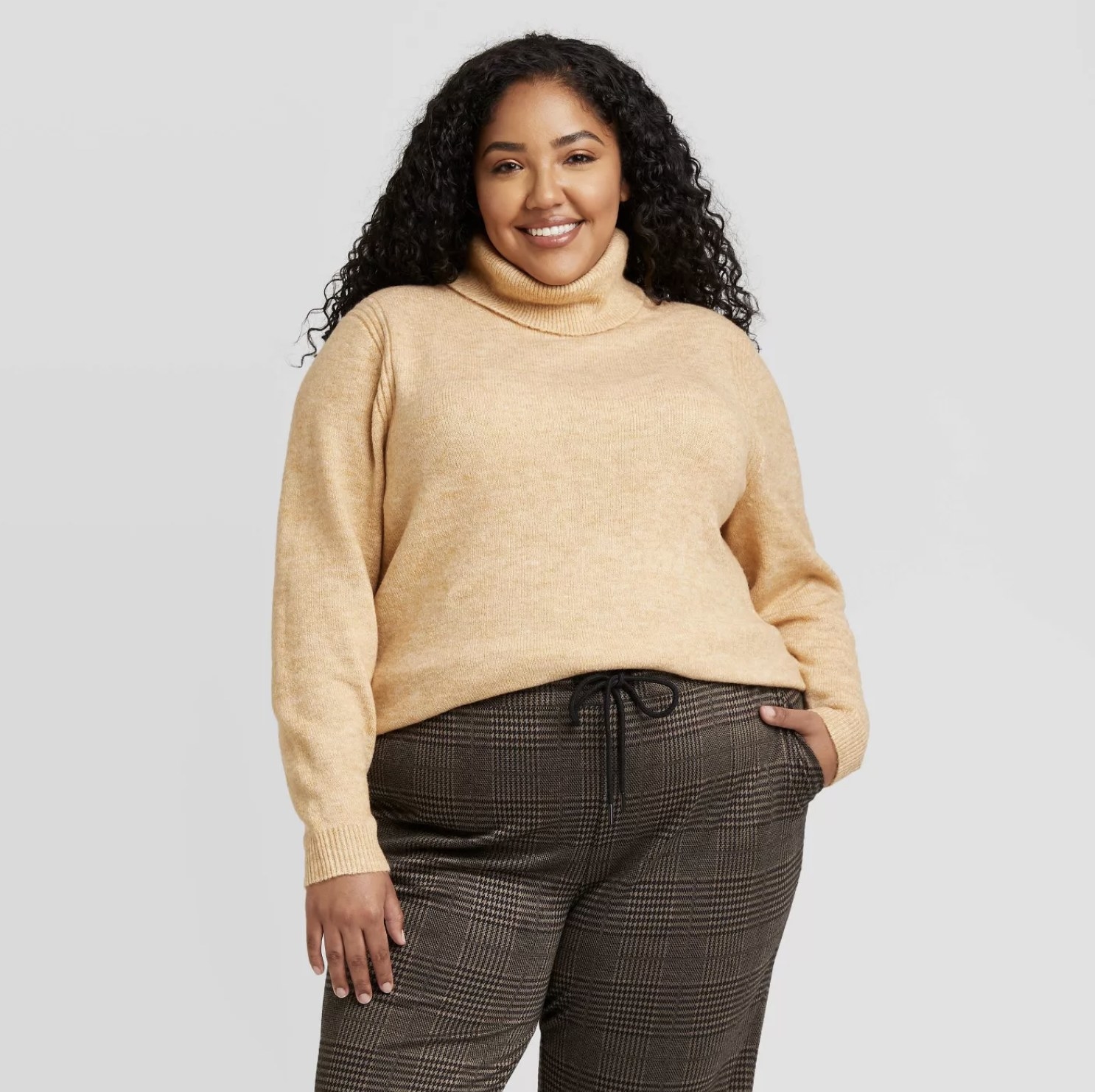 Model is wearing a cream pullover turtleneck sweater and plaid pants
