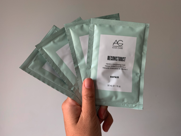 Liza&#x27;s hand holding several packets of the AG Reconstruct hair mask