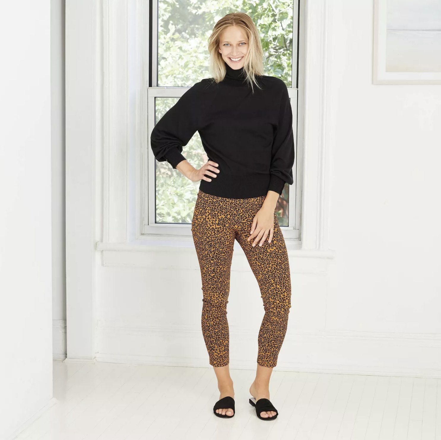 Model is wearing gold leopard print cropped pants, a black turtleneck sweater, and black slides