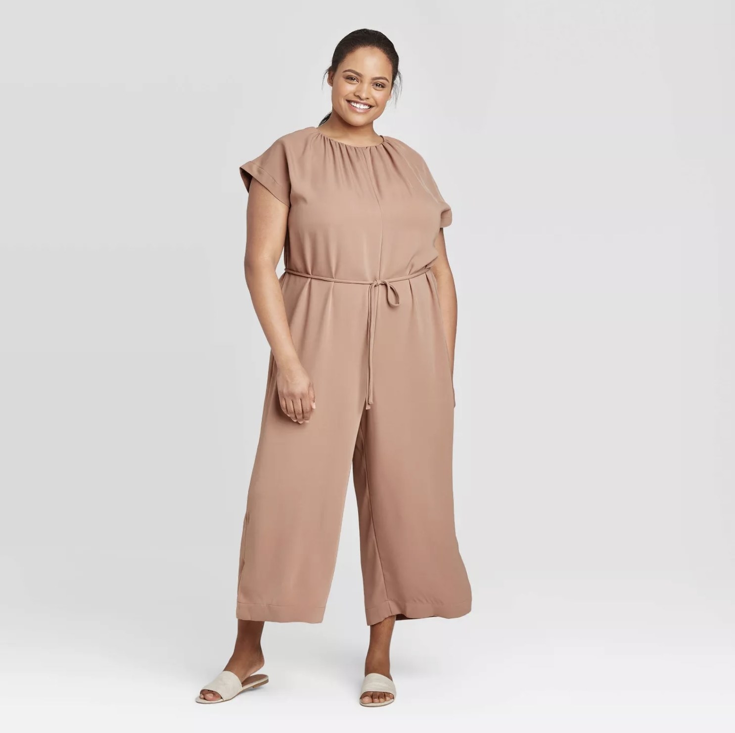 Model is wearing a mauve short sleeve ankle length jumpsuit with gathered waist details and grey slides