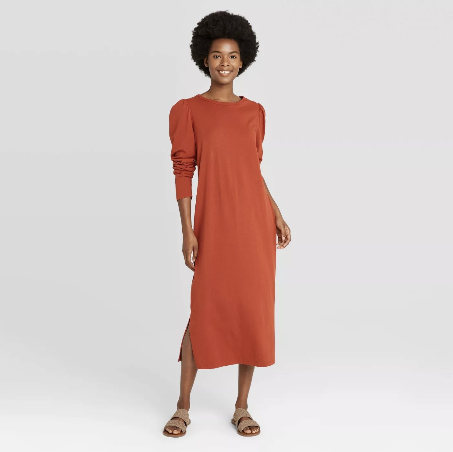 Model is wearing a rust orange long sleeve midi dress with puffed sleeves and tan slides