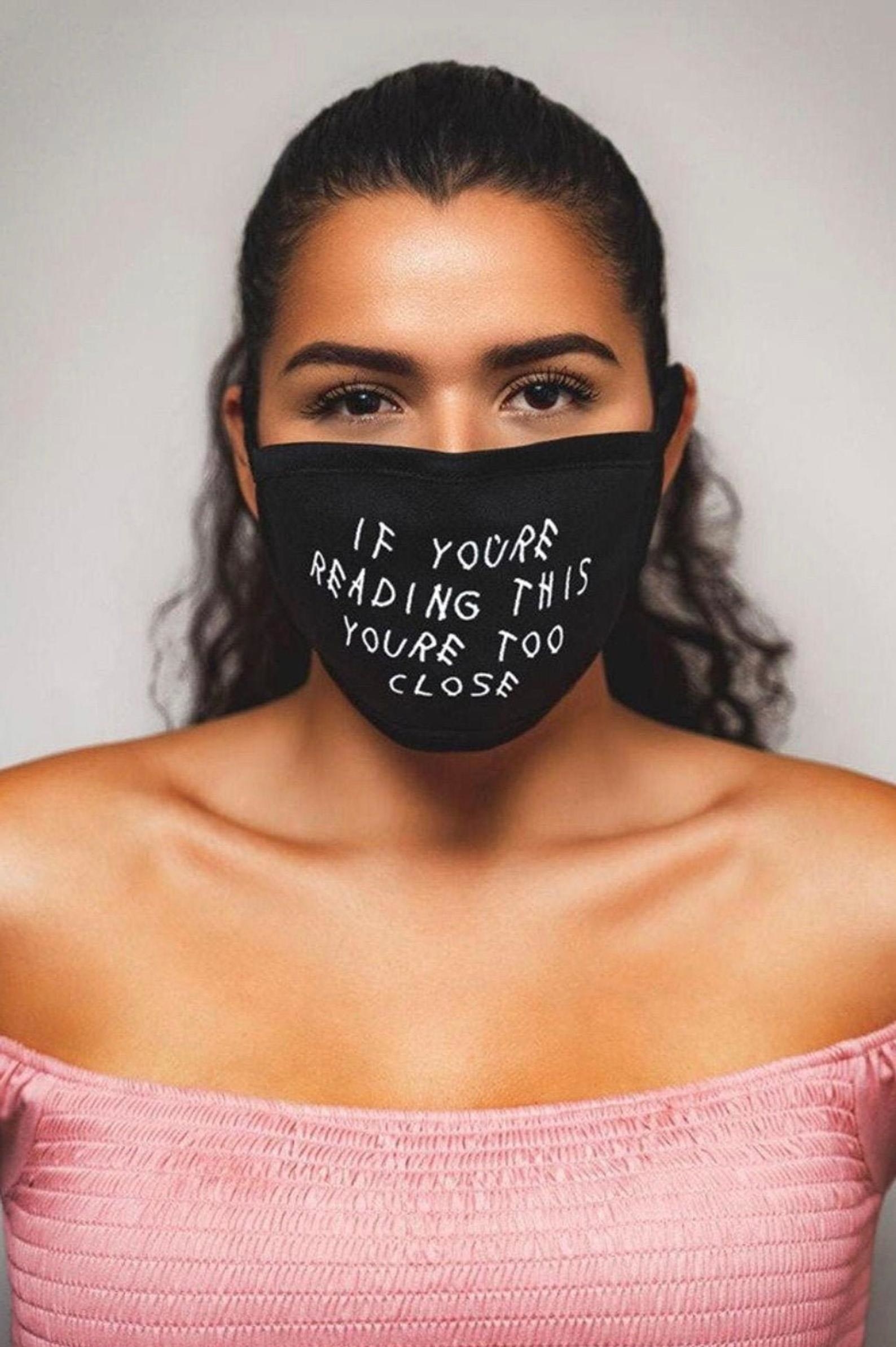 A black face mask that says &quot;if you&#x27;re reading this you&#x27;re too close&quot; in white 