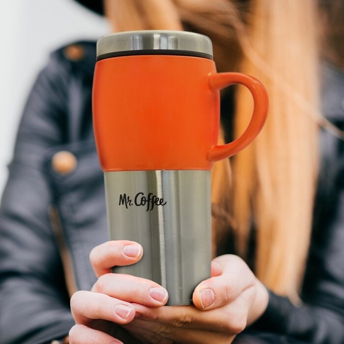 Model holding the travel mug in orange 