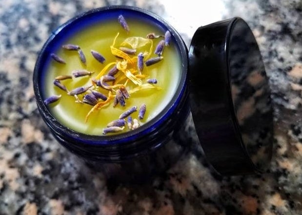 A tub of the balm topped with herbs or petals