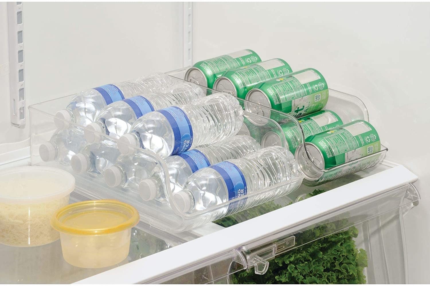 Two plastic bins filled with bottles of water and  pop cans on the top shelf of a refrigerator