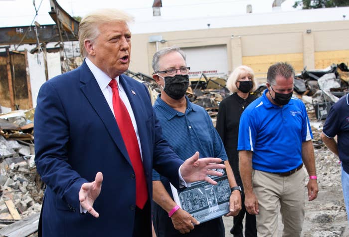 Trump talks while standing with people wearing facemasks near the remains of a building