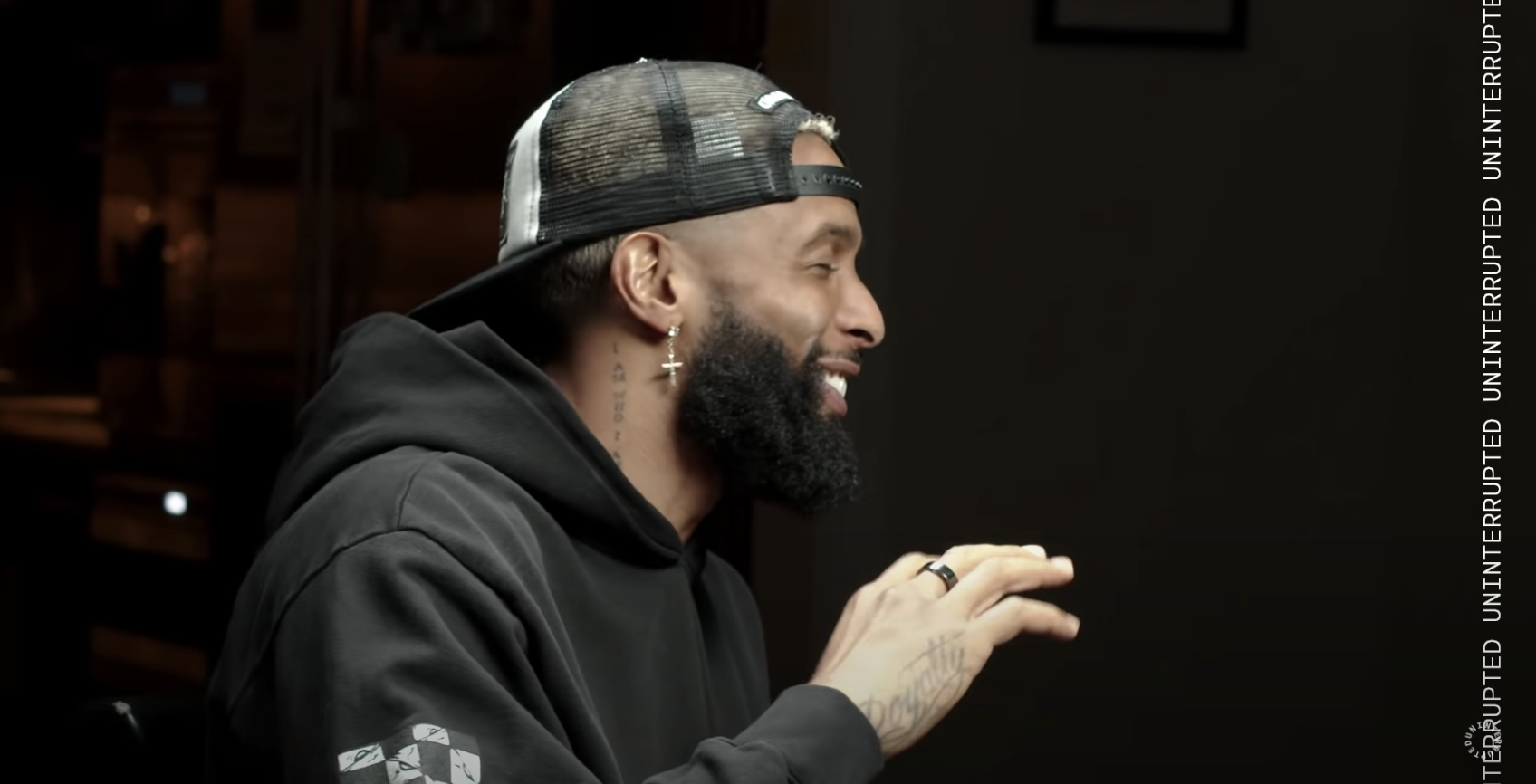 Odell laughs wearing a dark hoodie and dark hat