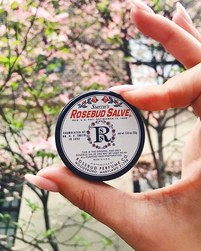A model holding a tin of the rosebud salve