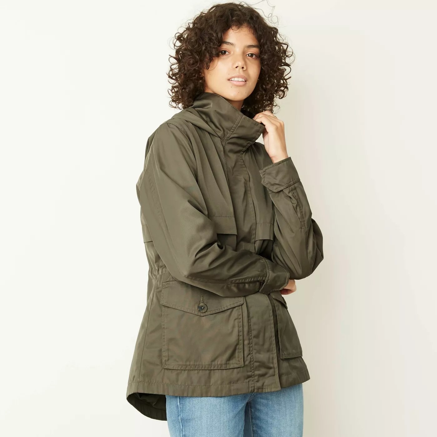 A model wearing a zipped-up rain jacket with a high neck and large, buttoned pockets