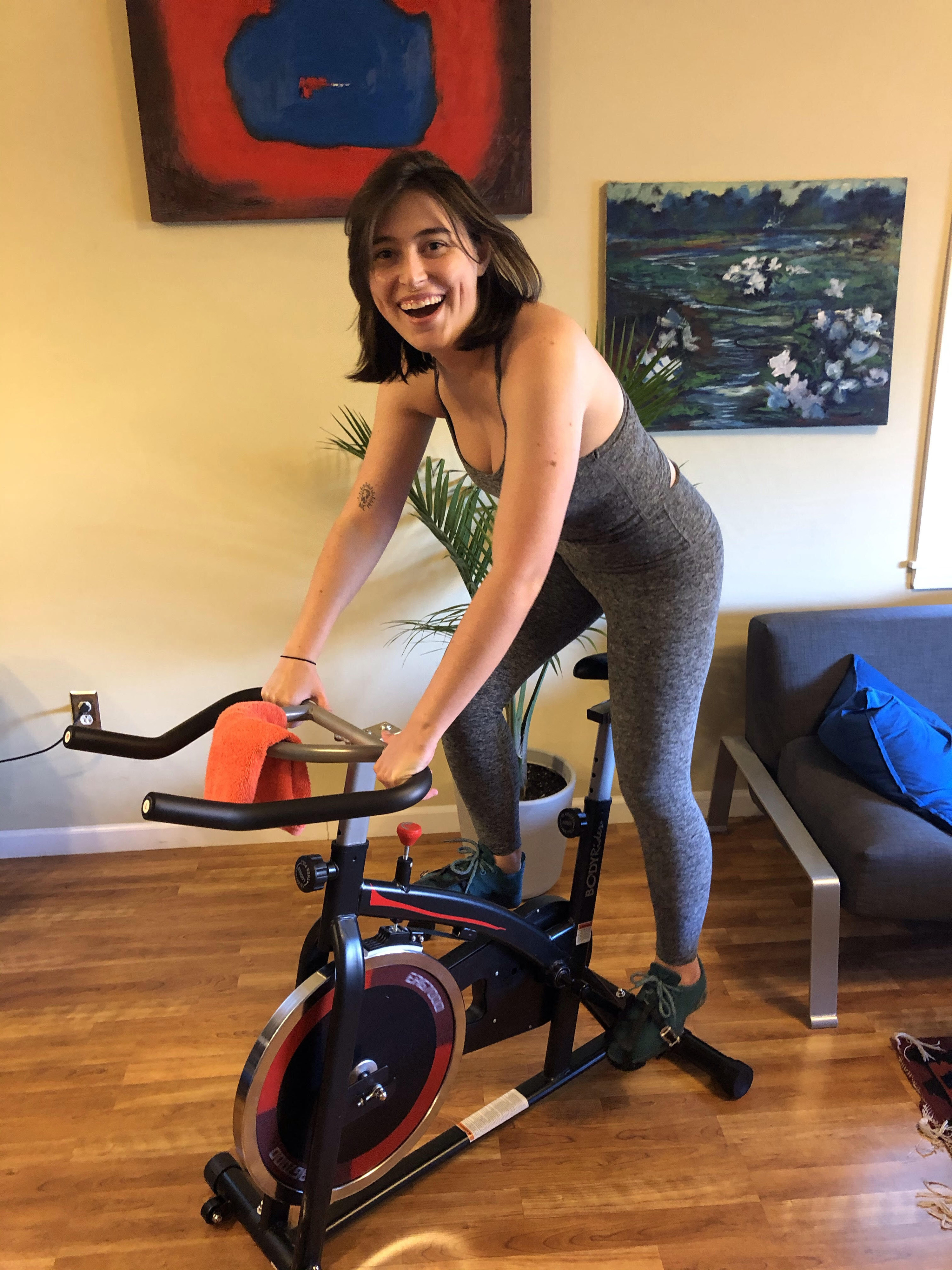 BuzzFeed writer Rachel Dunkle wearing the grey cropped tank top and leggings while riding a stationary bike.