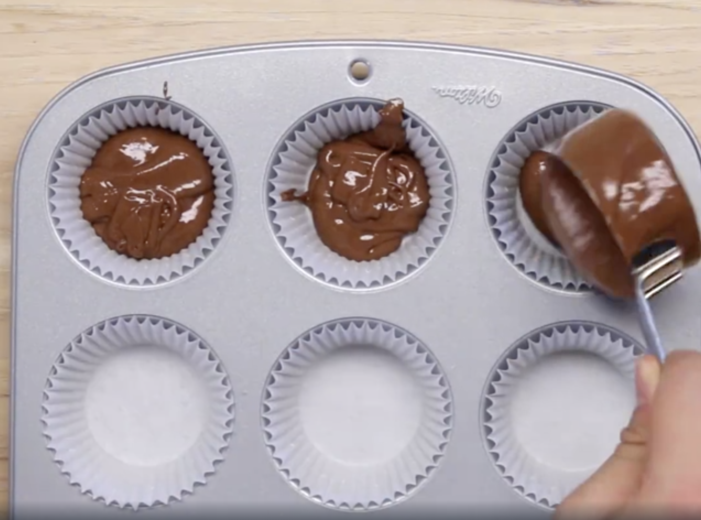 Cupcake batter being scooped into a cupcake tin.