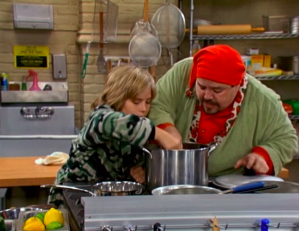 Zack and Chef Paolo dip pieces of chocolate into a large pot of gravy in the hotel kitchen.