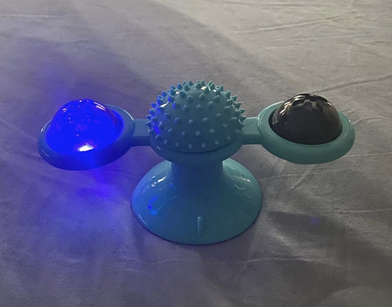 a turquoise spinning toy with a spiked center, with two rotating LED balls (one of which is lit blue)