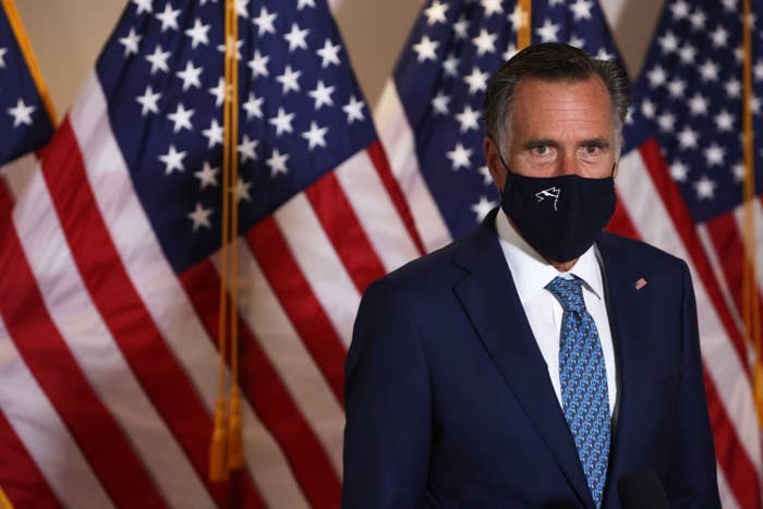 Romney wears a face mask in front of several American flags 