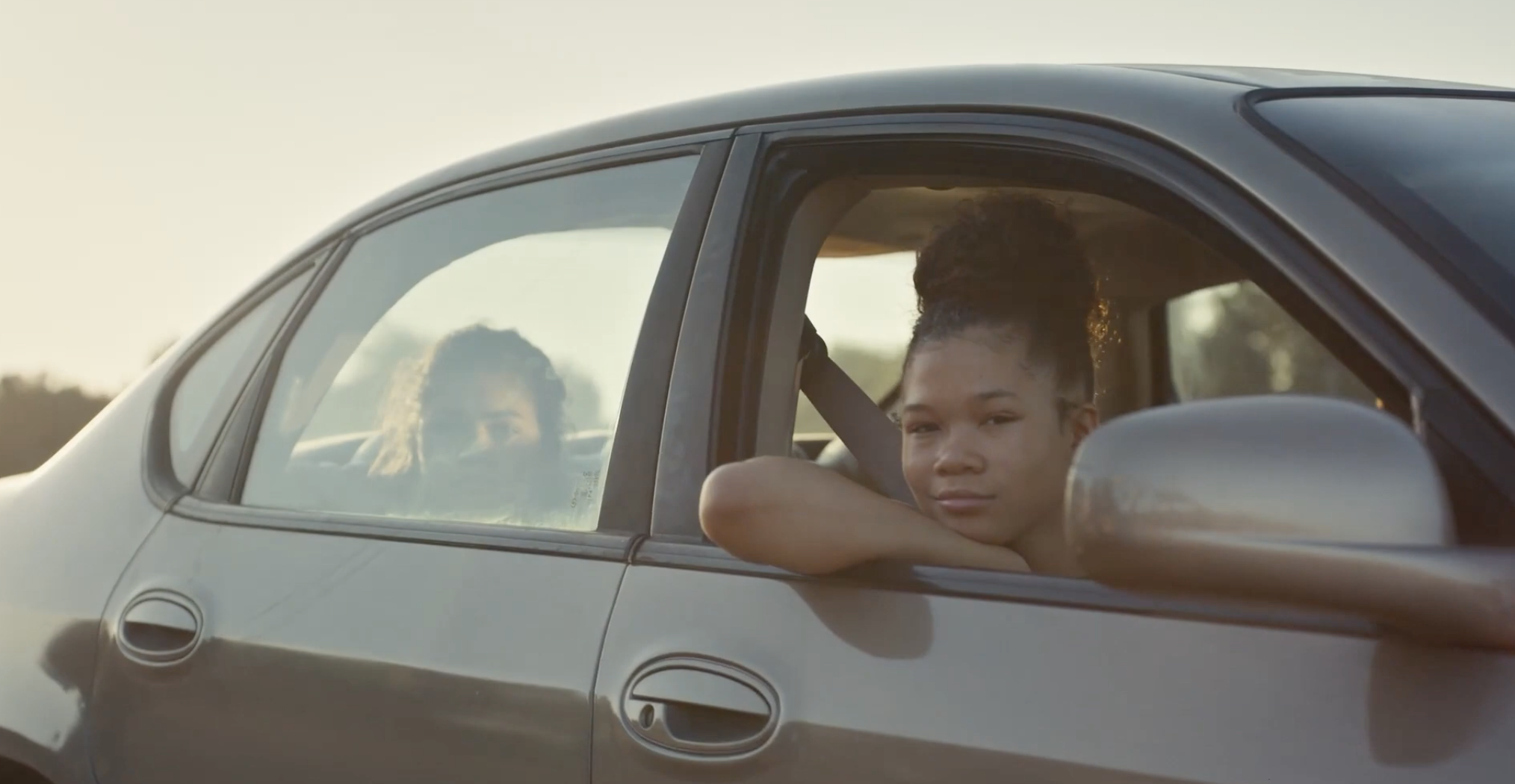 Gia and Rue looking out at Jules riding her bike from a car window