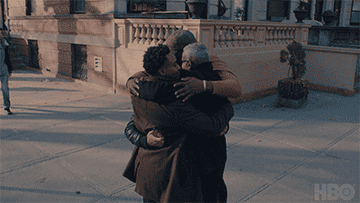 A bunch of Black men of all ages hug on a street corner
