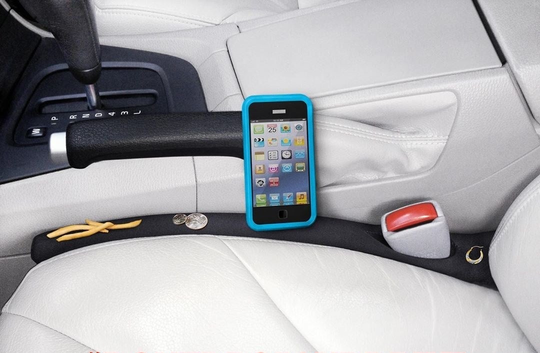 A long fabric block placed between a car seat and the console with fries, coins, and a phone on top of it