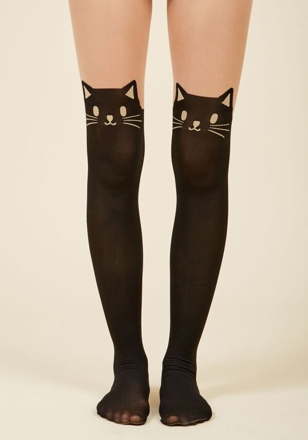 A model wearing the tights, which are sheer on top and black on the bottom, with a black cat face design at the knee