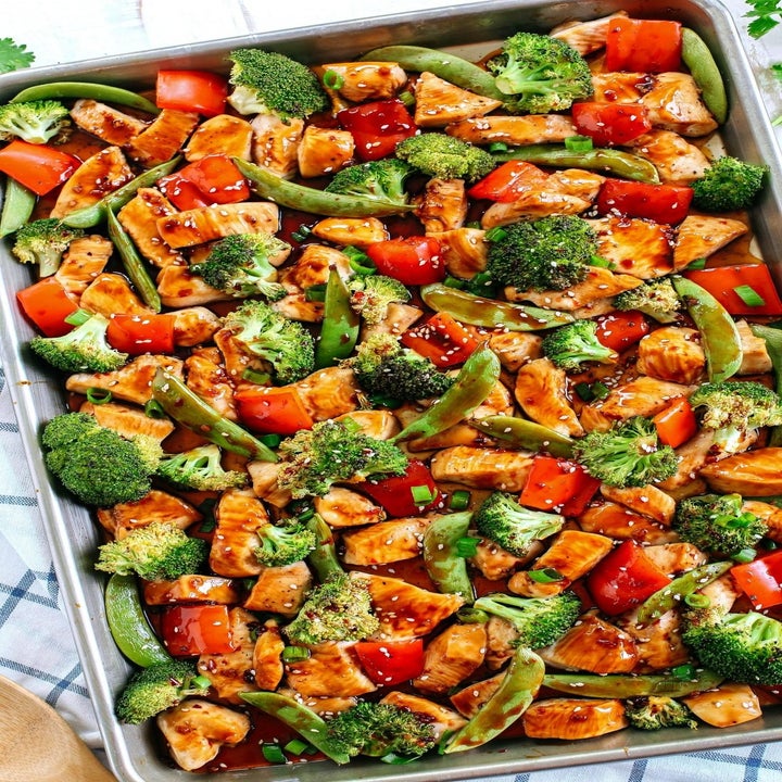 A sheet pan topped with sesame chicken, snap peas, broccoli, and peppers.