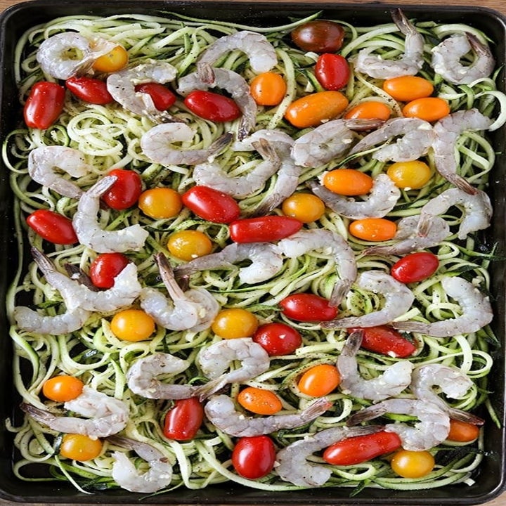 Raw shrimp, cherry tomatoes, and spiralized zucchini on a sheet pan.
