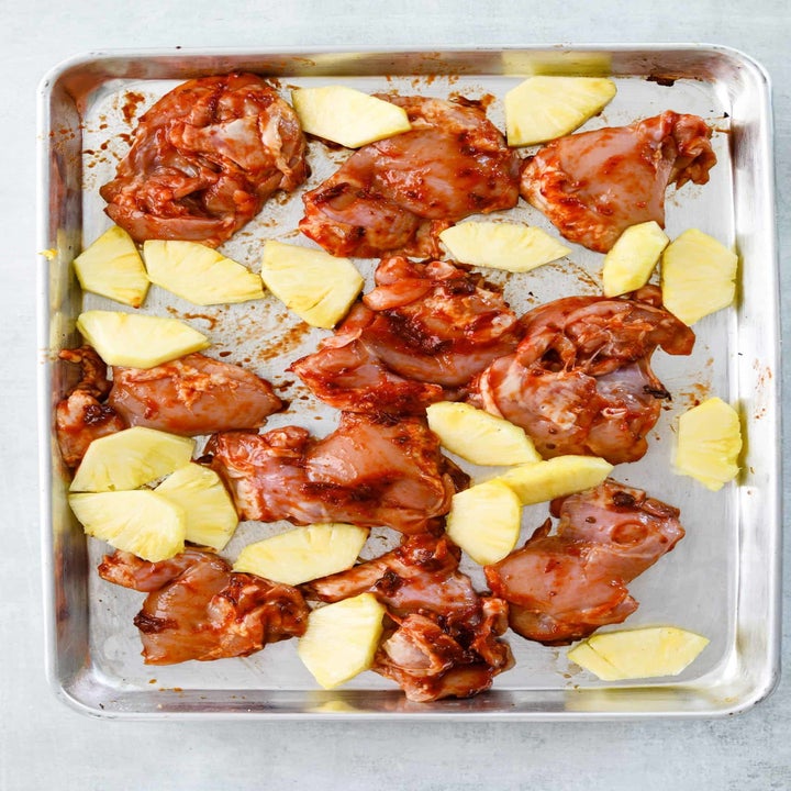 Marinated chicken and sliced pineapple on a sheet pan.