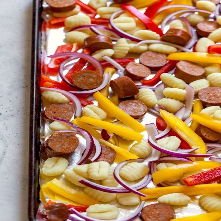 Potato gnocchi, sliced sausage, peppers, and onion on a sheet pan.