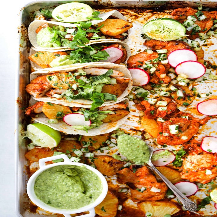 A sheet pan of chicken al pastor tacos, topped with radishes, guacamole, fresh herbs, and lime wedges.