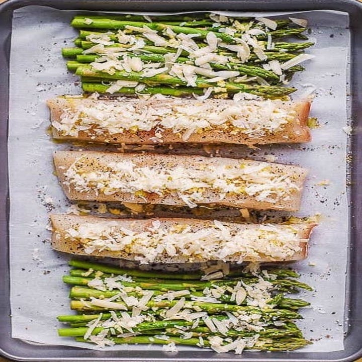 Uncooked halibut fillets with asparagus on a sheet pan.