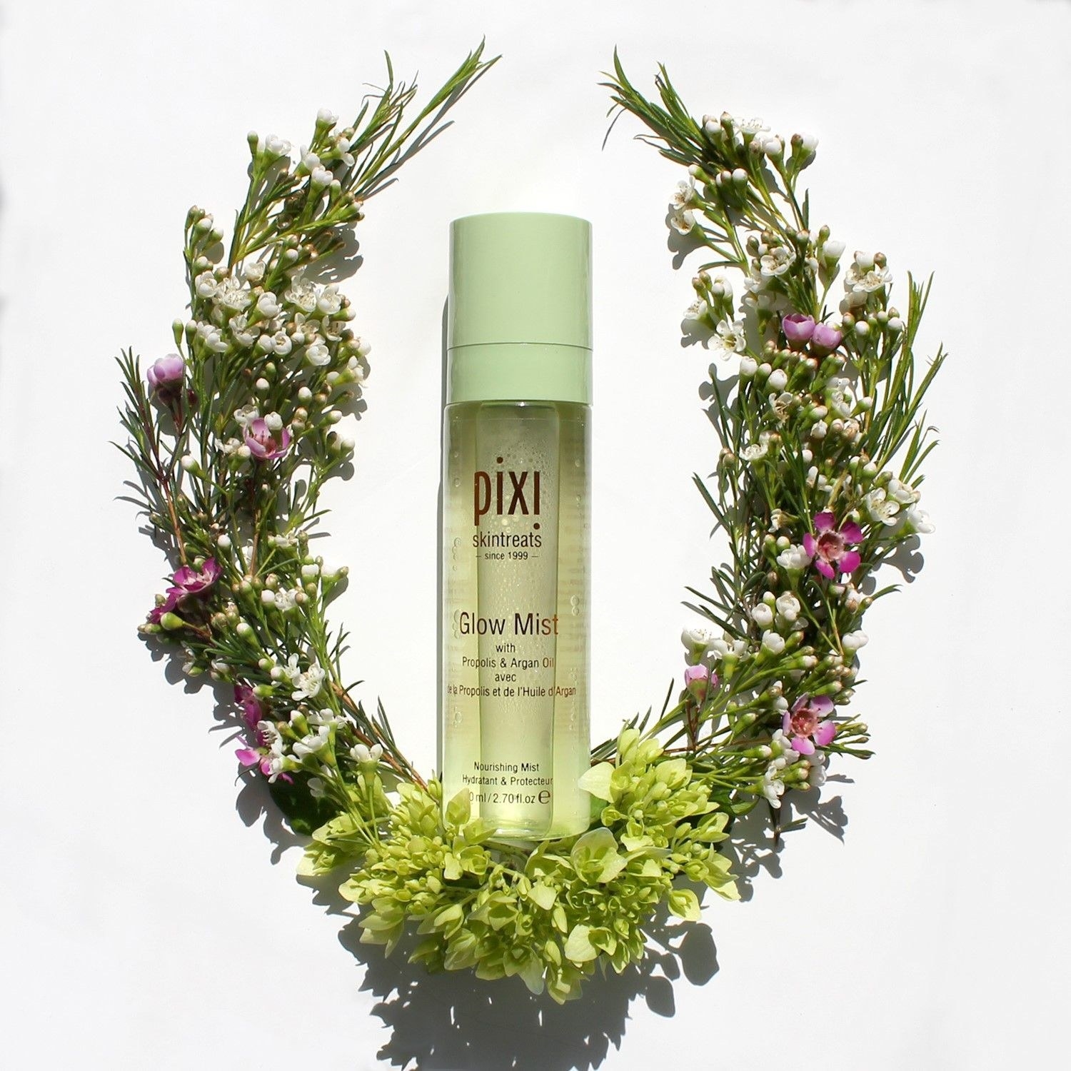 a bottle of glow mist surrounded by a floral wreath 