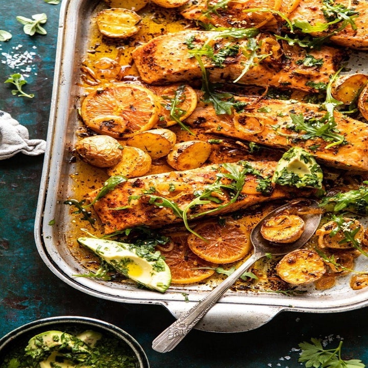 A sheet pan topped with cooked salmon and potatoes in a citrus sauce with herbs.