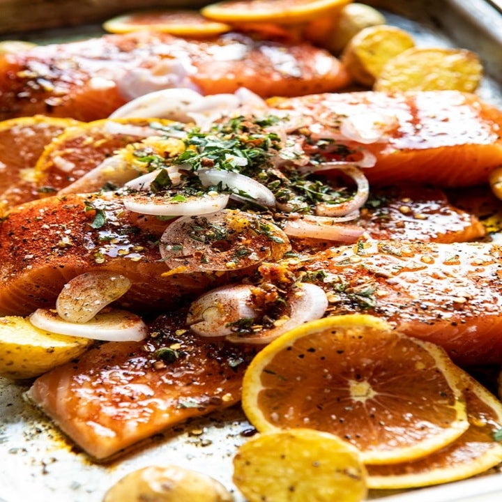 Raw salmon fillets covered in citrus and herbs with chopped potatoes on the side.