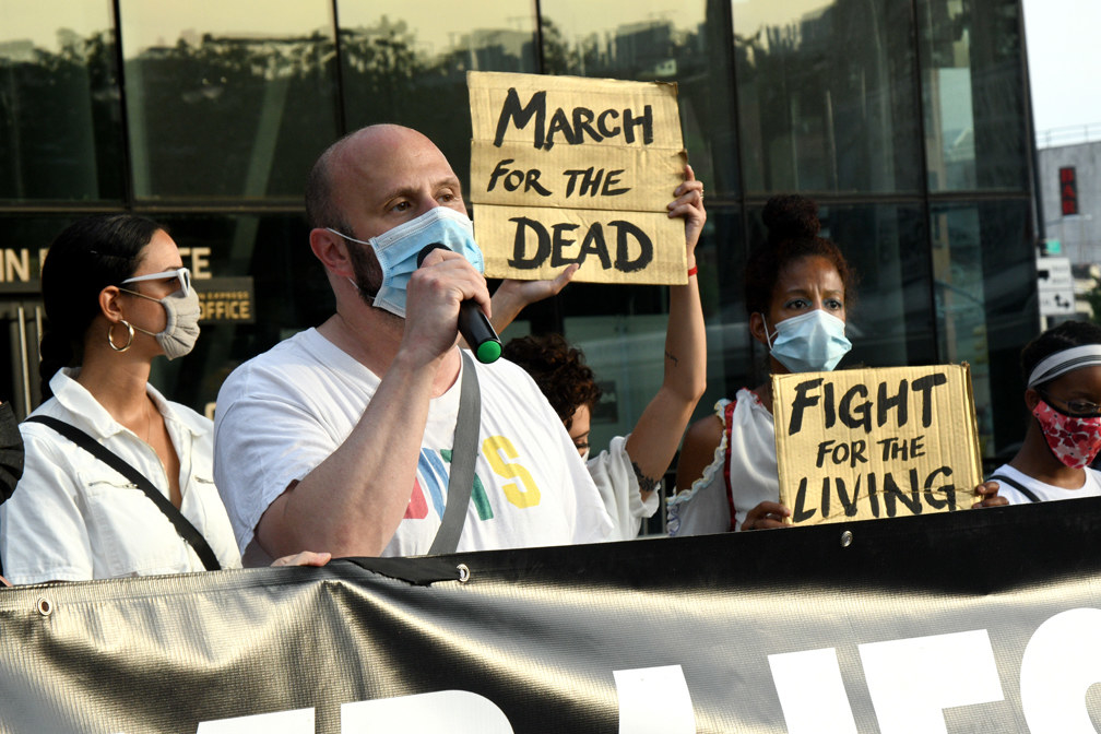 Protesters wearing masks hold signs reading &quot;March for the Dead&quot; and &quot;Fight for the living.&quot;