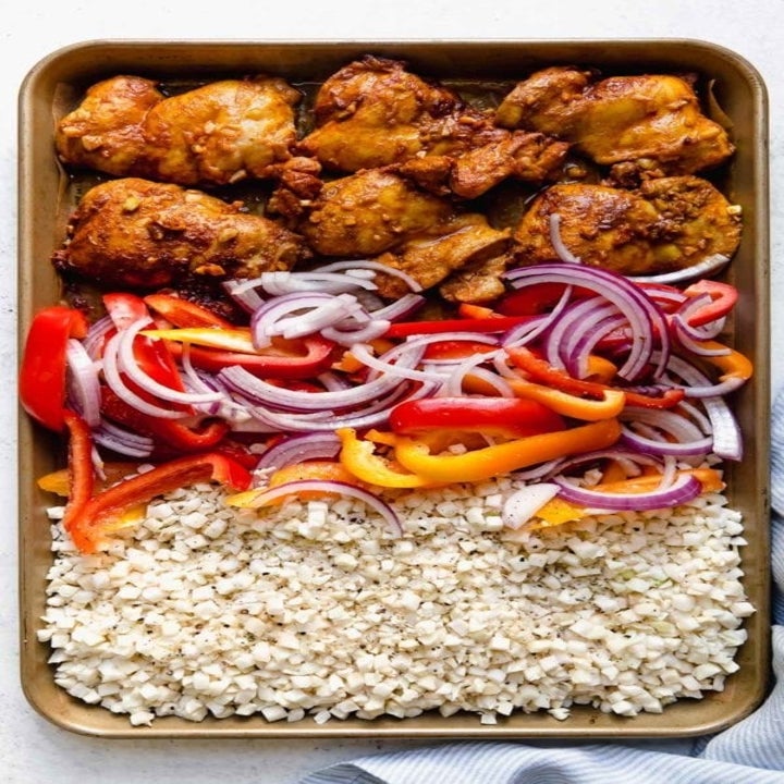 A sheet pan with marinated chicken, peppers and onions, and cauliflower rice.
