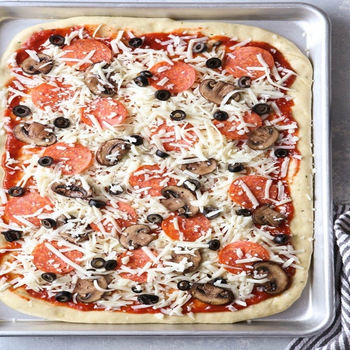 An uncooked sheet pan pizza with cheese and veggie toppings.