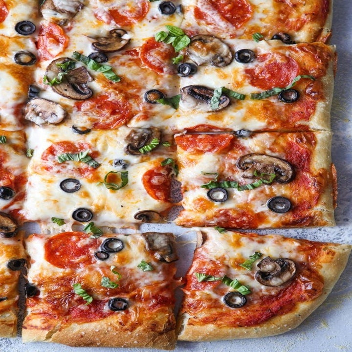 A sheet pan pizza topped with cheese, tomato sauce, olives, pepperoni, and mushrooms.