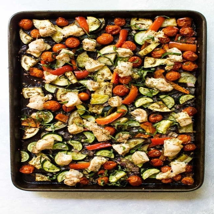 A sheet pan topped with little pieces of chicken and chopped tomatoes, zucchini, eggplant, and peppers.