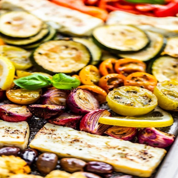Roasted tomatoes, olives, zucchini, and feta cheese on a sheet pan.