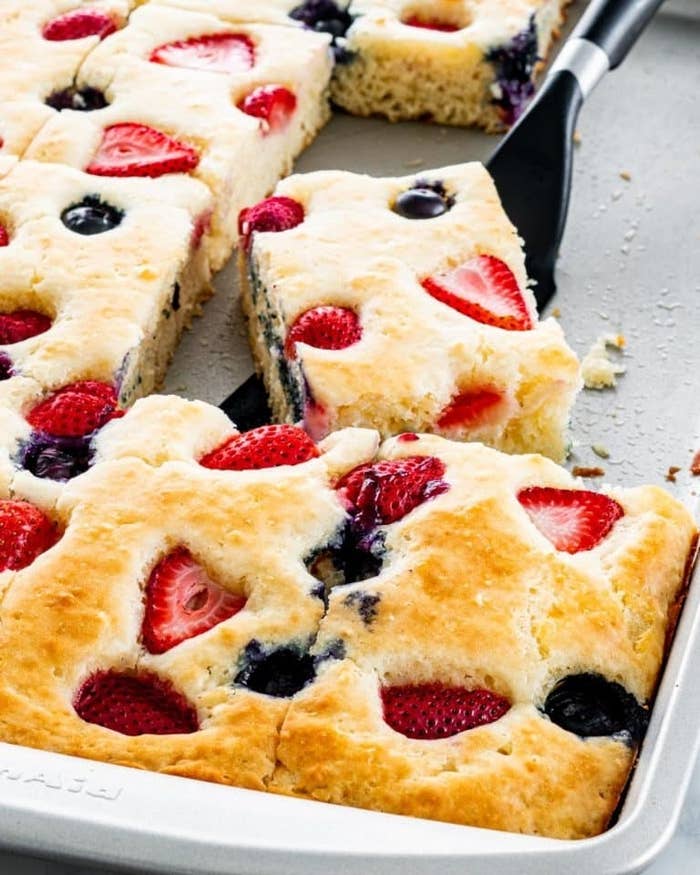 Sheet pan pancakes filled with strawberries and blueberries being sliced into squares.