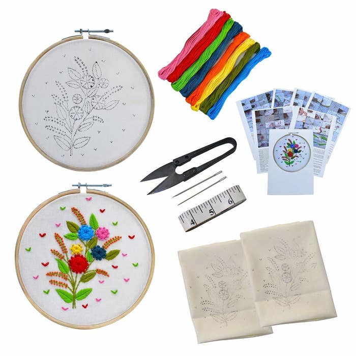 The embroidery kit pictured with needles, embroidery thread, measuring tape, embroidery scissors, cloth, tutorial booklet, and an embroidered hoop.