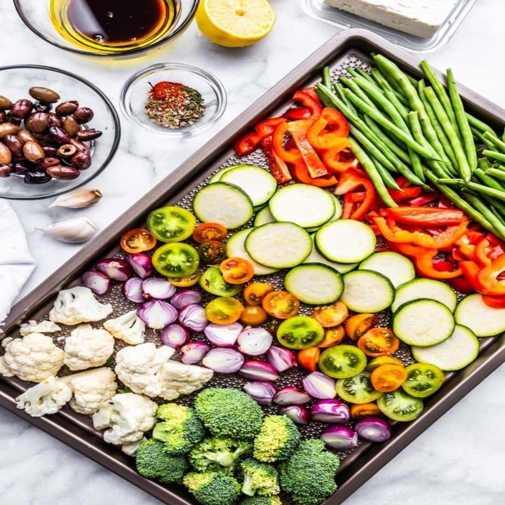 A sheet pan with sliced tomatoes, zucchini, green beans, peppers, broccoli, and cauliflower.