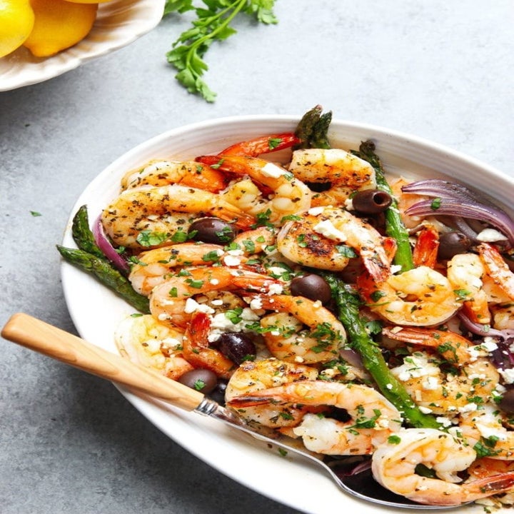 A serving tray topped with shrimp and veggies with crumbled feta.