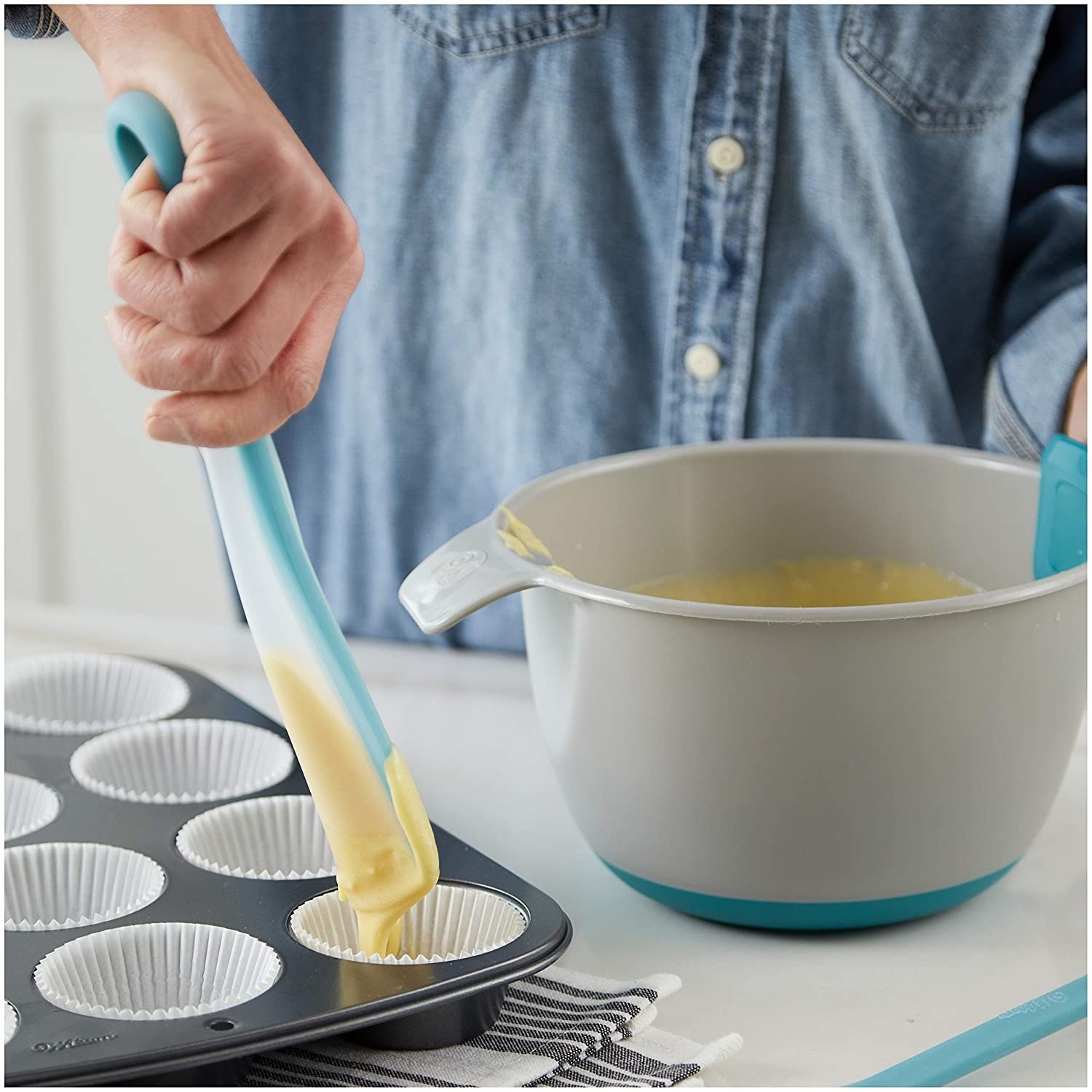 A person squeezing the spatula and scooping cupcake batter into a muffin tin