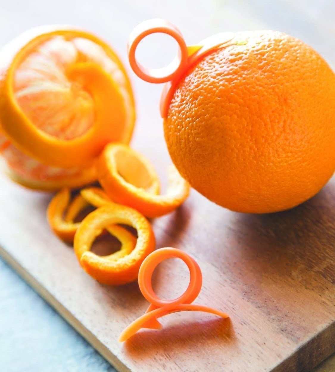 A peeled orange and an orange wit the peeler dug into it on a cutting board