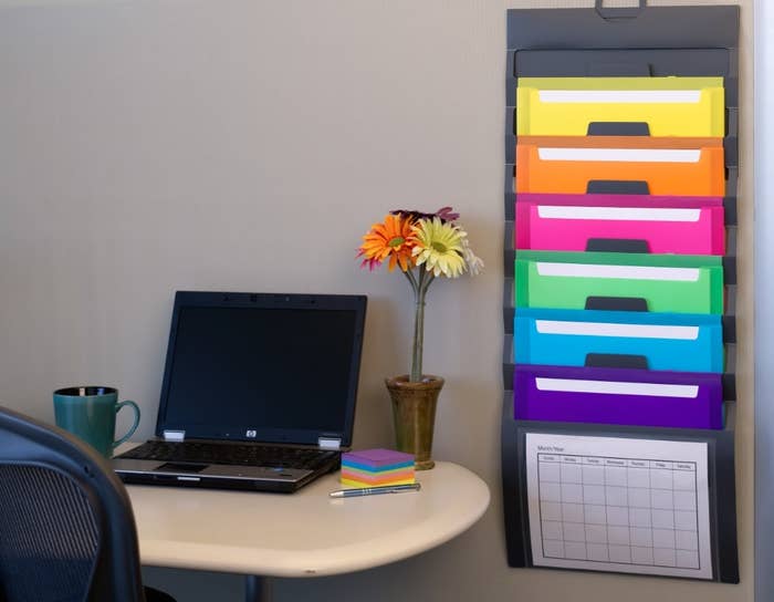 The colorful organizer hung next to a desk with a computer and flowers